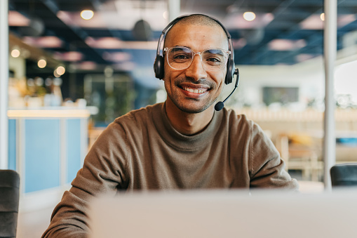 Businessman wearing eyeglasses and headset smiling cheerfully at camera in call center office