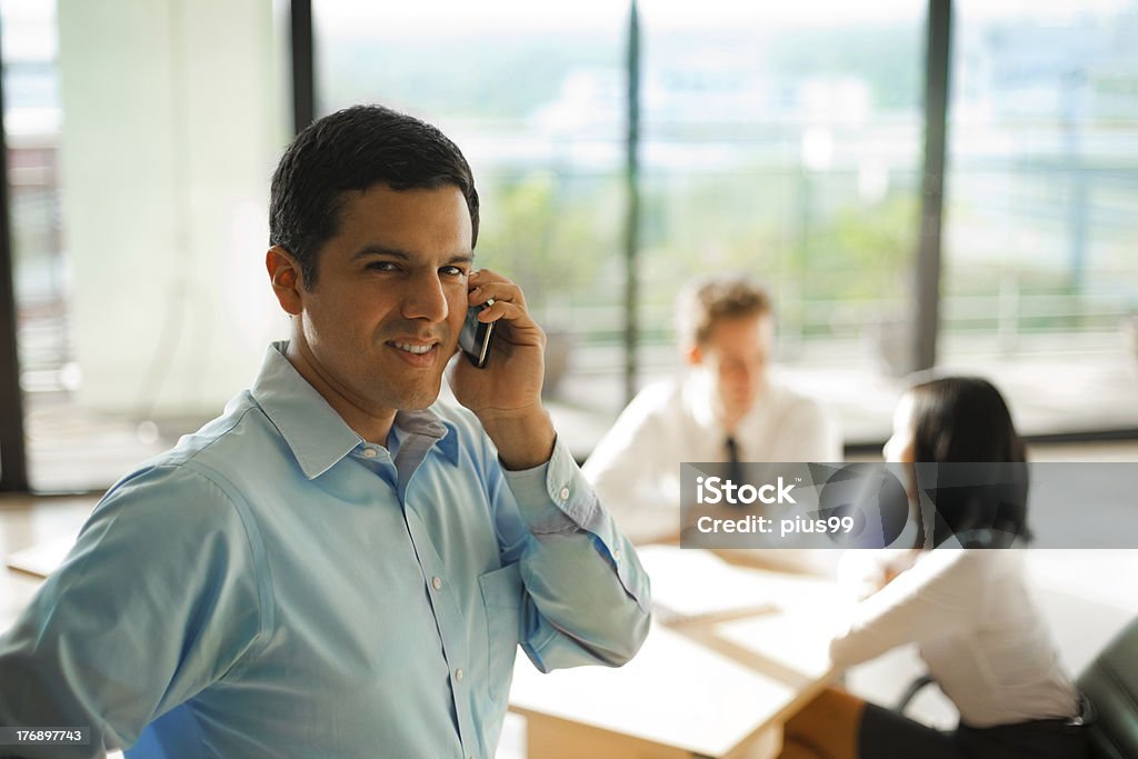 Latino Man Phone Call Business Meeting A latino male answers a phone call during a business meeting with his colleagues Business Stock Photo