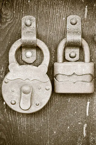 Old padlocks on an ancient rural house entrance door.Sepia conversion.