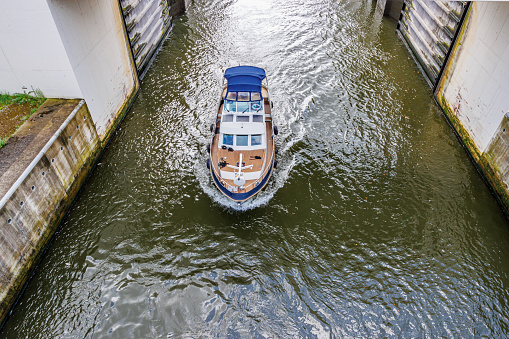 Top angle of a small boat leaving the Lanaye lock with the floodgate open towards the Albert canal, huge walls with low water level, cloudy summer day in Ternaaien, Belgium