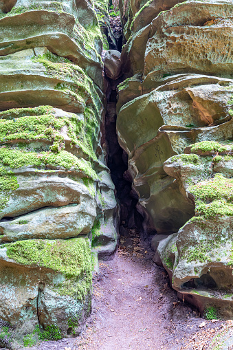 Narrow furrow between two walls with different shapes of abrasion on huge moss-covered rock formations in Teufelsschlucht nature reserve, rocks in background, sunny summer day in Irrel, Germany