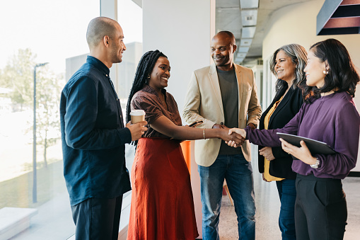 Multiracial group of business partners shaking hands, smiling and getting to know each other in coworking office space