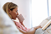Young woman reading book on bed at home