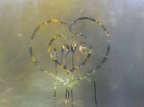 a heart painted on condensation-covered glass. inside is the word love in English. symbol of love, fidelity, sympathy. drops flow down the glass. broken, unreciprocated love