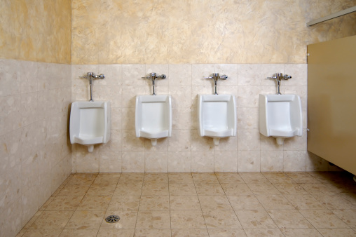 A collection of 4 urinals in a men's bathroom with the one on the far left a little lower than others.