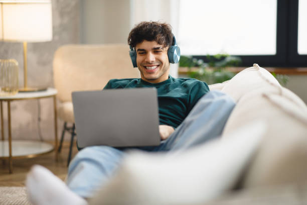 istock Cheerful Middle Eastern Guy Using Laptop Wearing Headphones At Home 1769051517