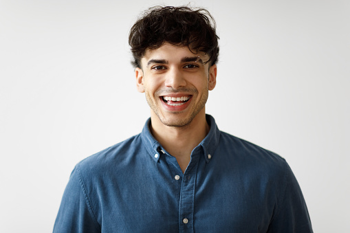 Portrait Of Happy Middle Eastern Guy With Eyebrow Piercing Ring Posing Over White Studio Background. Handsome Arabic Young Man In Casual Clothing Smiling To Camera Expressing Positive Emotions