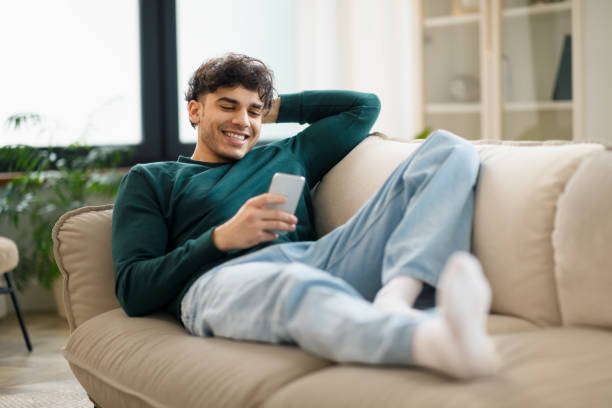 istock Guy Browsing Internet On Smartphone Lying On Couch At Home 1769051540