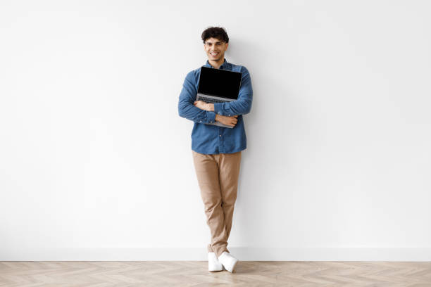 istock Arab Guy Holding And Hugging Laptop Standing Indoor, Full Length 1769052085