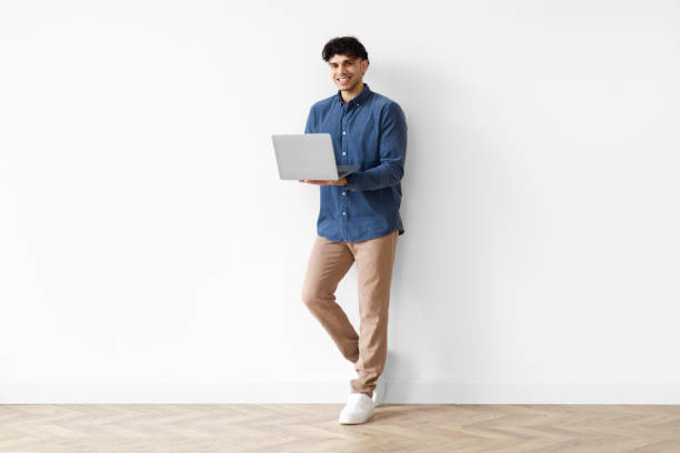 istock Cheerful Middle Eastern Man Holding Laptop Working Online Standing Indoor 1769052120