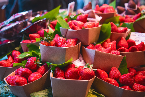 Close up. Eco-friendly cardboard boxes with strawberries for tourists at a Spanish market Mercado de La Boqueria. Juicy fresh sweet red strawberrys on the counter.