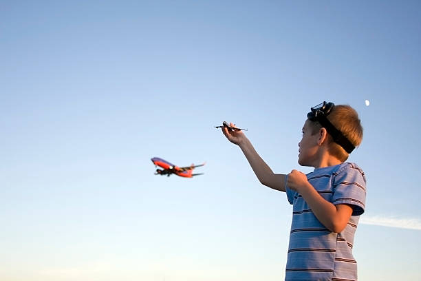 Young boy planes with toy airplane as real plan flies by.