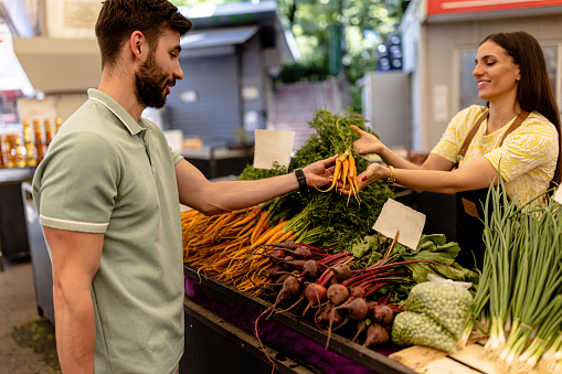 Embracing the garden-to-table ethos, the woman sells a variety of locally grown vegetables to a health-conscious shopper, emphasizing freshness, nutritional value, and supporting the local farming community at the street market