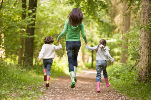 Mother and daughters skipping on woodland path smiling