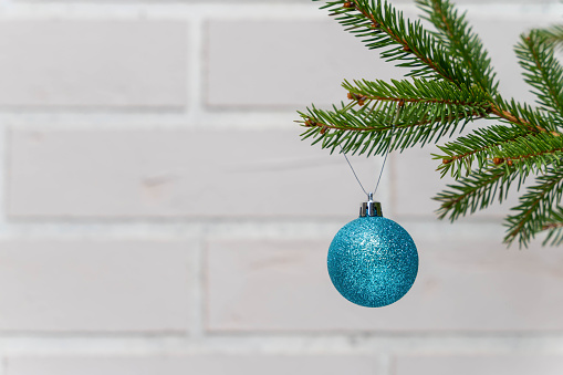a blue Christmas ball on the branches of a Christmas tree against a white brick wall. The concept of celebrating the New Year. copy space