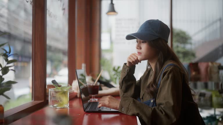 Asian young woman having coffee and working using a laptop at a cafe .