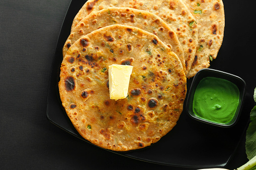 Healthy Indian Mooli or Radish paratha or stuffed flatbread with coriander and green chilies on wooden background