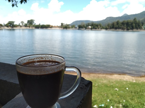 A glass of black coffee with a lake in the background