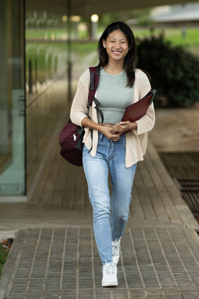istock Handsome satisfied student walking outside holding a notebook looking at camera. Relaxed and happy woman standing outside with files on her hands. 1769103286