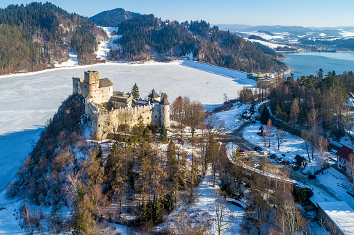 Niedzica, Poland - February 14, 2022:  Medieval castle in Niedzica, dating back to 14th century (upper castle) in winter. Frozen artificial Czorsztyn lake on Dunajec river and a dam
