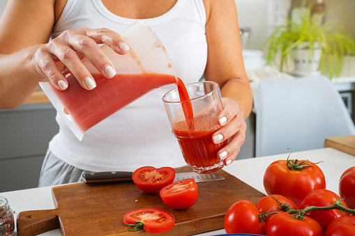 Close up of woman hands pouring fresh tomato juice to a glass for a healthy breakfast