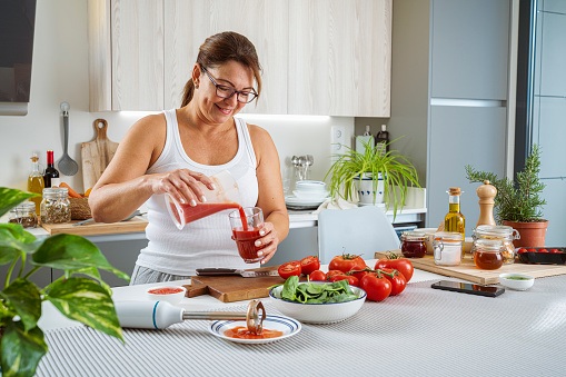 Woman pouring fresh tomato juice to a glass for a healthy breakfast