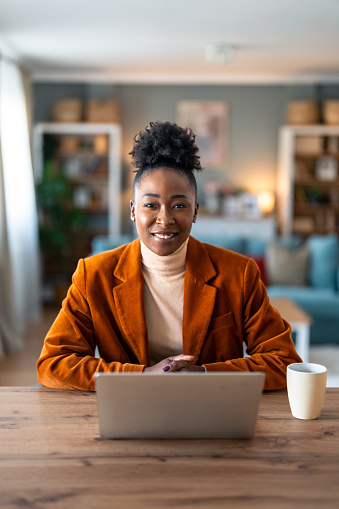 Smiling confident businesswoman looking at camera sitting at home office desk. Modern stylish female corporate employee successful executive manager with laptop posing for business portrait.