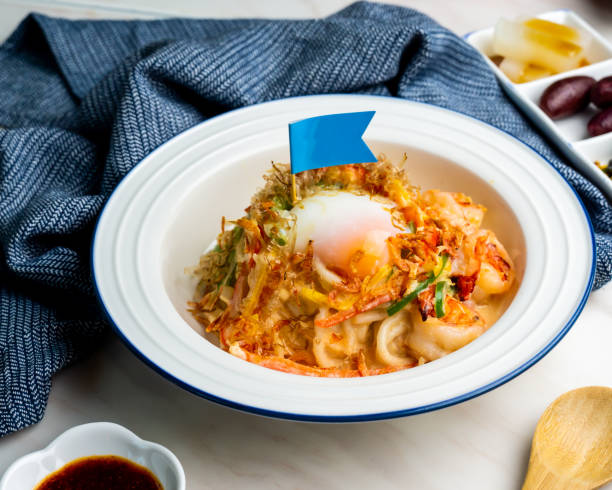 タイ風スパイシーなミックスフィッシュうどんは、ナプキンの側面から見た丼で提供され、テーブルの上の日本食