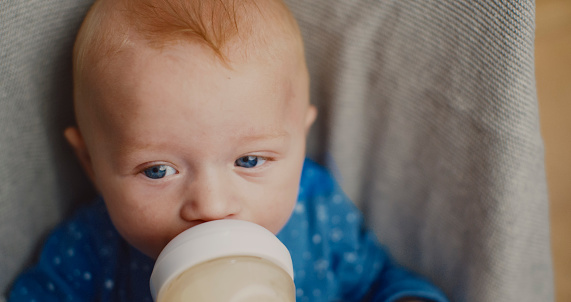 A pensive baby boy enjoys a bottle of milk in his bouncer,portraying innocence and introspection in this endearing close-up.