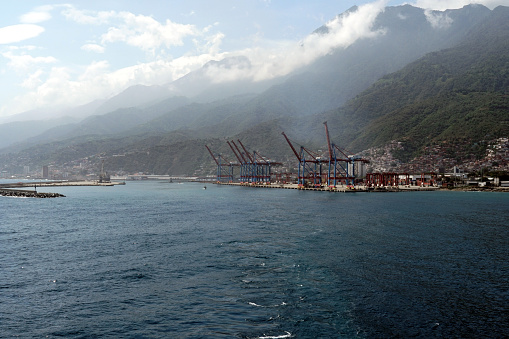 La Guaira, Venezuela, 05 12 2023: Modern container terminal with gantry cranes in Port of La Guaira observed from cargo ship approaching Venezuela coats. Seaport is situated among green mountain.