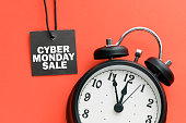 CYBER MONDAY SALE words on a small tag and red background with a clock. View from above.