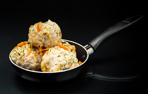cooked chicken diet meatballs in a frying pan, isolated on a black background