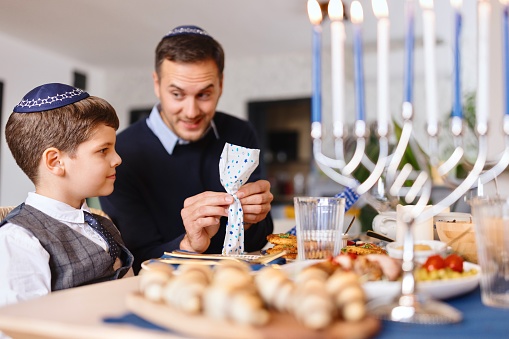 Close-up of a Jewish father and son opening gift during traditional Hanukkah dinner
