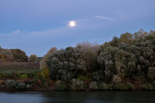 Autumn riverbank at sunset with the rising moon in the background.