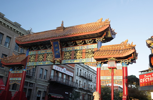 Victoria, Canada - September 18, 2023: Low angle view of the Gate of Harmonious Interest spanning Fisgard Street in Victoria's Chinatown National Historic Site. Summer morning with a clear sky over southern Vancouver Island.