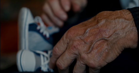 Timeless connection,A close-up view of the wrinkled hand of a grandfather tenderly holding his baby boy's tiny legs at home. A beautiful symbol of generations united