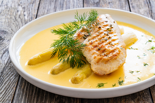 Grilled chicken breast and white asparagus in hollandaise sauce on wooden table