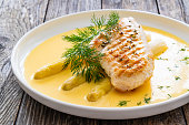 Grilled chicken breast and white asparagus in hollandaise sauce on wooden table