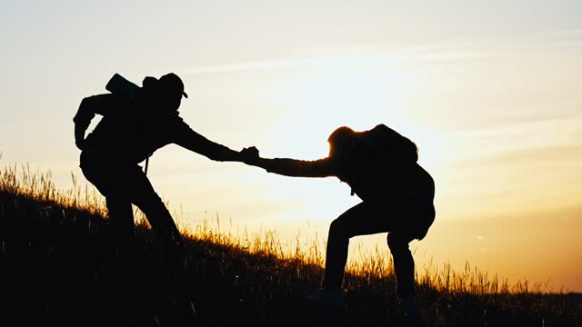 Silhouette of a helping hand to the man mountaineer. Two hikers on top of the mountain, a man helps a man to climb. Two hiker helping on hiking trail to summit the top of mountain. Teamwork concept.