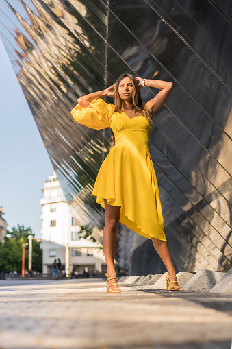 Vertical photo with low angle view of a sensual model posing with a yellow summer dress outdoors