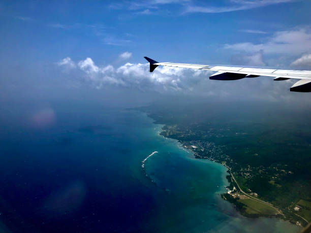 Airbus A321 flying over the Atlantic Ocean. The ocean is blue and the sky has a blue with small clouds. The Jamaican coast has beaches and forests with trees with green leaves.