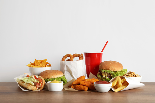 French fries, burgers and other fast food on wooden table against white background