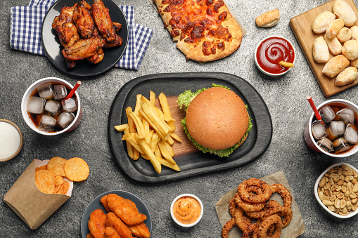 French fries, burger and other fast food on gray textured table, flat lay