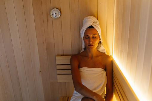 Woman relaxing in the hot sauna at her home bathroom.