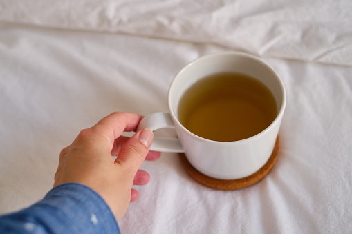 White cup with coffee or tea on the bed. Cozy morning photo. The concept is cozy and warm. Place for text
