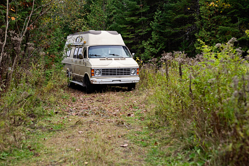 Vintage camper van on a dirt road in autumn forest. No people. Horizontal full length outdoors shot with copy space. This is part of a series and was taken in Quebec, Canada.