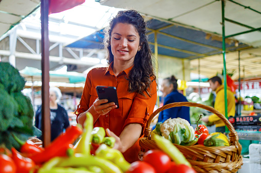 While shopping in a market, a mid-adult woman appears to be searching for organic or pesticide-free vegetables, aligning with health-conscious choices