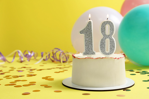 Coming of age party - 18th birthday. Delicious cake with number shaped candles on yellow background, space for text