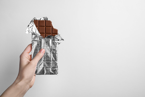 Woman holding delicious chocolate bar on white background, closeup. Space for text