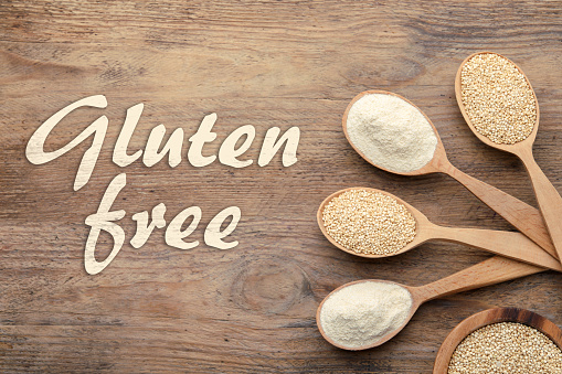 Gluten free products. Spoons with different types of flour and text on wooden table, top view